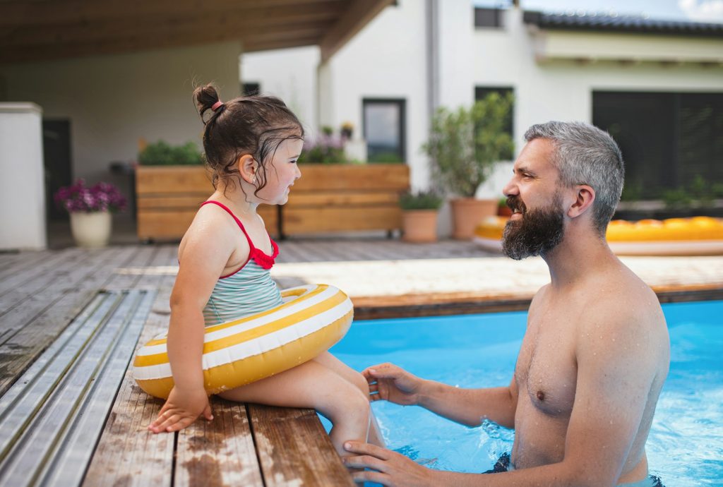 Father with daughter outdoors in the backyard, playing in swimming pool